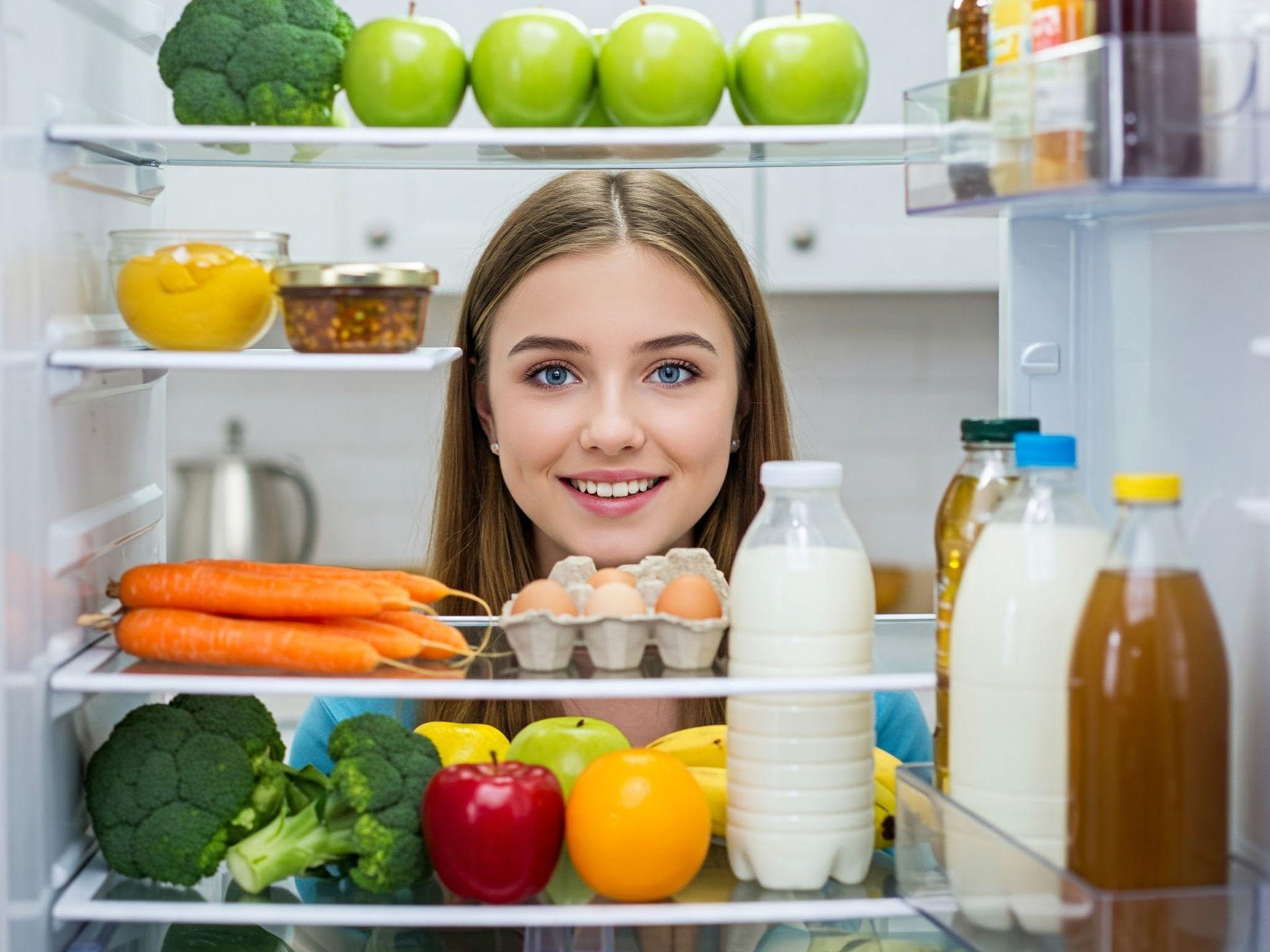 Ragazza sorridente sceglie cibo salutare dal frigorifero, un passo importante per la dieta.